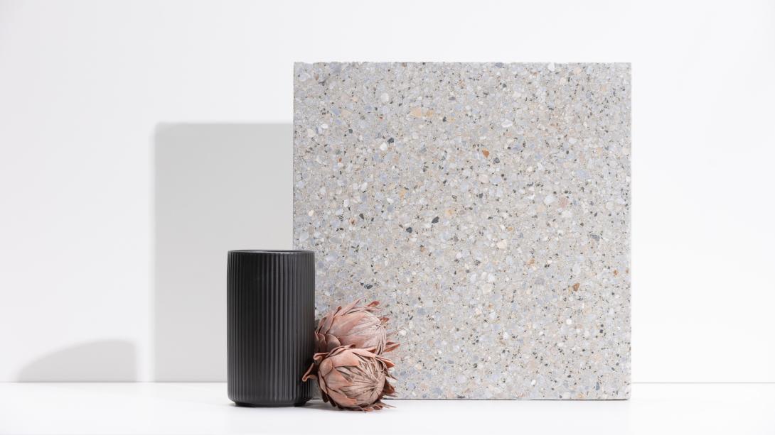 Slab of boralstone concrete in the colour Riverbed next to a black vase with dusty pink flowers
